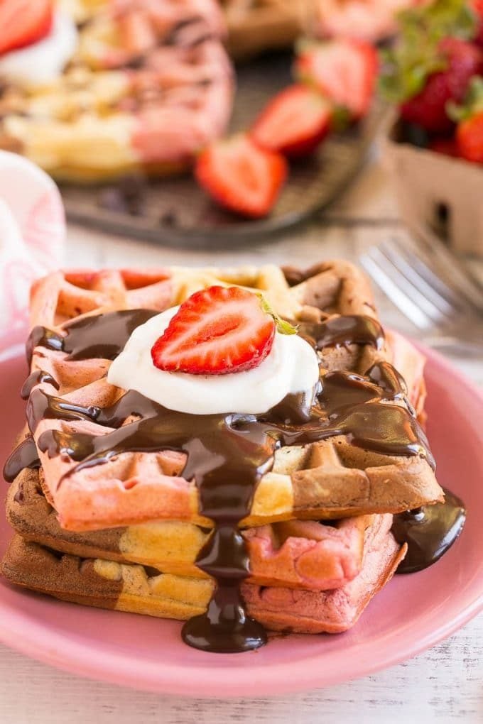 A stack of neopolitan waffles topped with chocolate sauce and berries.