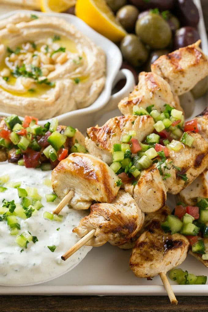 Greek Chicken Souvlaki Recipe | Easy Greek Chicken | Chicken Souvlaki | Greek Chicken Skewers | Easy Greek Chicken Skewers #chicken #kabobs #glutenfree #keto #lowcarb #grilling #edsug A tray of chicken souvlaki kabobs with olives, hummus, pita bread and yogurt sauce.