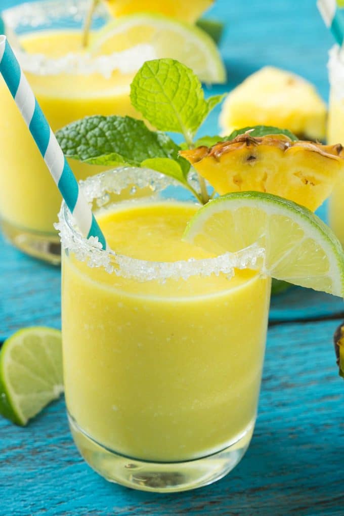 Pineapple Coconut Smoothie Recipe |Tropical Smoothie | Pineapple Smoothie #smoothie #pineapple #coconut #healthy #cleaneating #edsug A cup of pineapple smoothie with garnishes of lime, pineapple wedges and mint sprigs.
