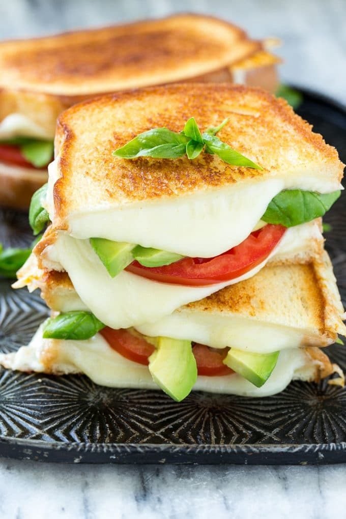 A caprese sandwich with toasted bread, tomatoes, mozzarella cheese, basil and avocado.