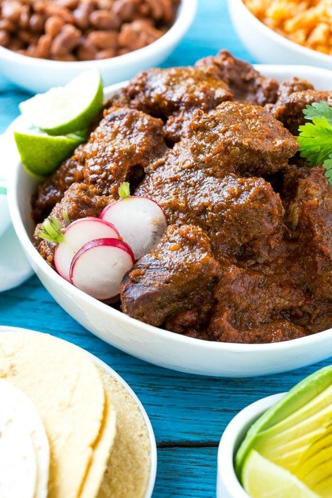 A bowl of chile colorado served with tortillas, beans and avocado.