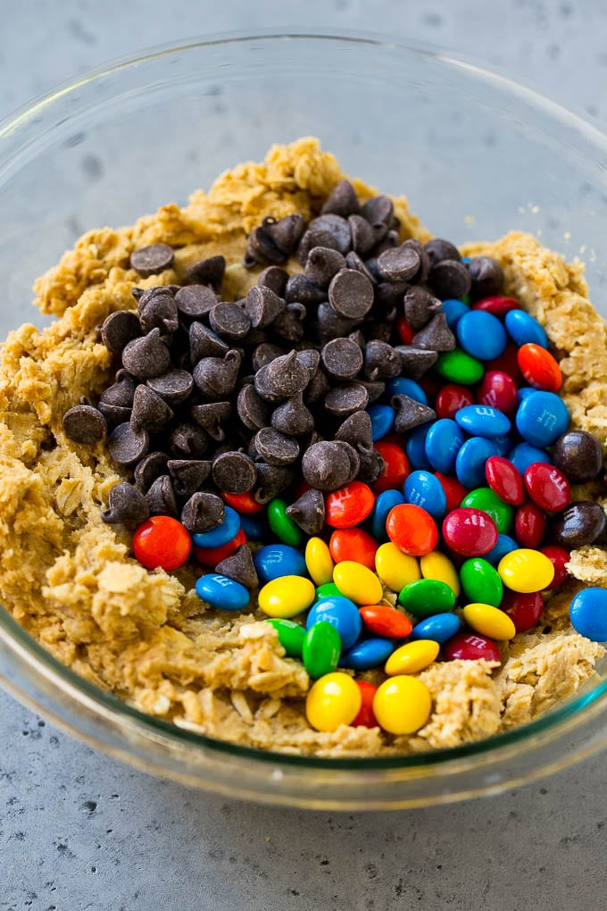 Monster Cookies Recipe | Oatmeal Cookies | Peanut Butter Cookies | M&M's Cookies #baking #cookies #dessert #peanutbutter #chocolate #edsug Cookie dough with chocolate chips and M&M's on top.