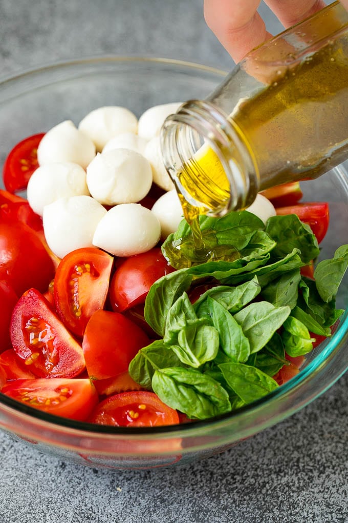 Caprese Salad Recipe | Tomato Salad #salad #tomato #mozzarella #cheese #basil #caprese #summer #edsug Olive oil being poured over tomatoes, mozzarella and basil leaves.