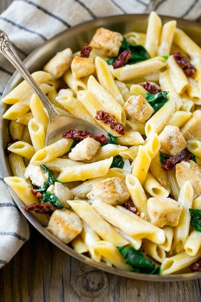 A pan full of sun dried tomato pasta with a serving spoon in it.