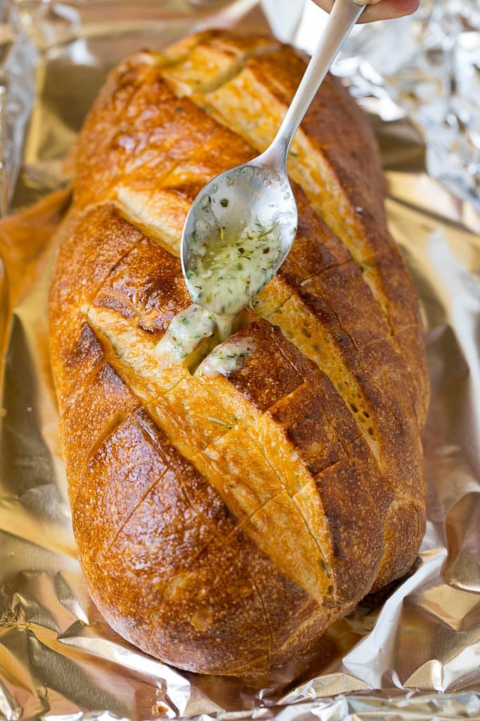 Pull Apart Bread | Garlic Bread | Cheese Bread #bread #garlic #cheese #sidedish #appetizer #edsug A spoon drizzling garlic butter over a loaf of bread.