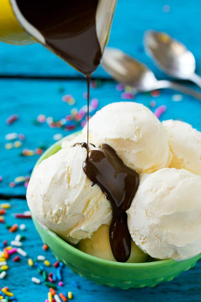 Homemade Magic Shell Recipe | Chocolate Ice Cream Topping | Chocolate Sauce | Hard Chocolate Coating #chocolate #icecream #dessert #edsug A pitcher of chocolate sauce being poured over vanilla ice cream.