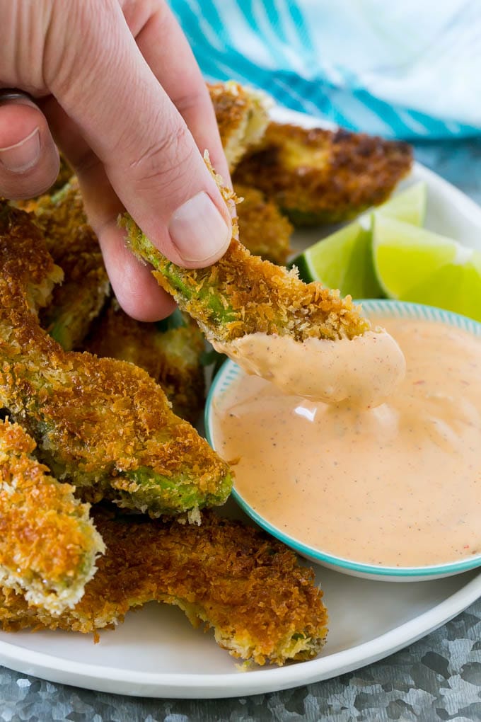 Avocado Fries Recipe | Fried Avocado | Avocado Fritters #avocado #appetizer #snack #edsug A hand dipping an avocado fry into sauce.
