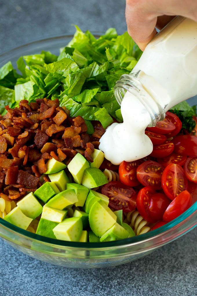 BLT Pasta Salad Recipe | Easy Pasta Salad | Bacon Pasta Salad #salad #pasta #blt #bacon #avocado #dinner #edsug Ranch dressing being poured over tomatoes, lettuce, bacon and avocado.