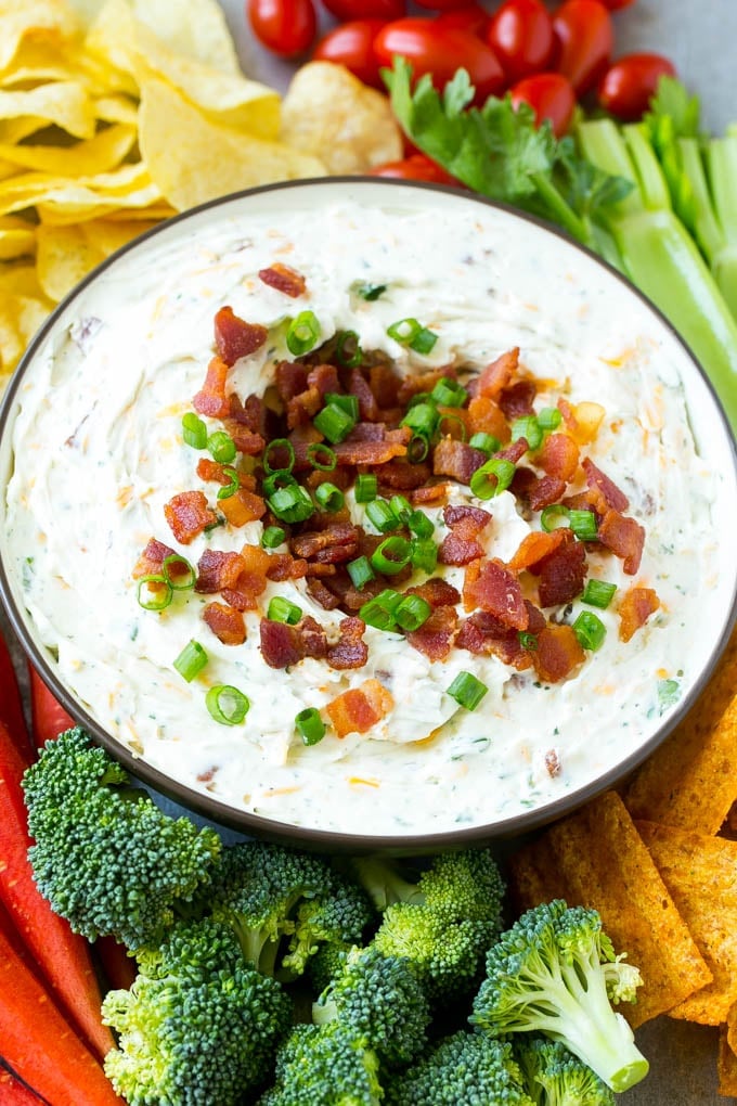 Bacon Ranch Dip Recipe | Homemade Ranch Dip | Easy Dip Recipe | Cheddar Ranch Dip #ranch #ranchdip #bacondip #dip #snack #edsug #baconranchdip A bowl of creamy bacon cheddar ranch dip surrounded by vegetables and chips.