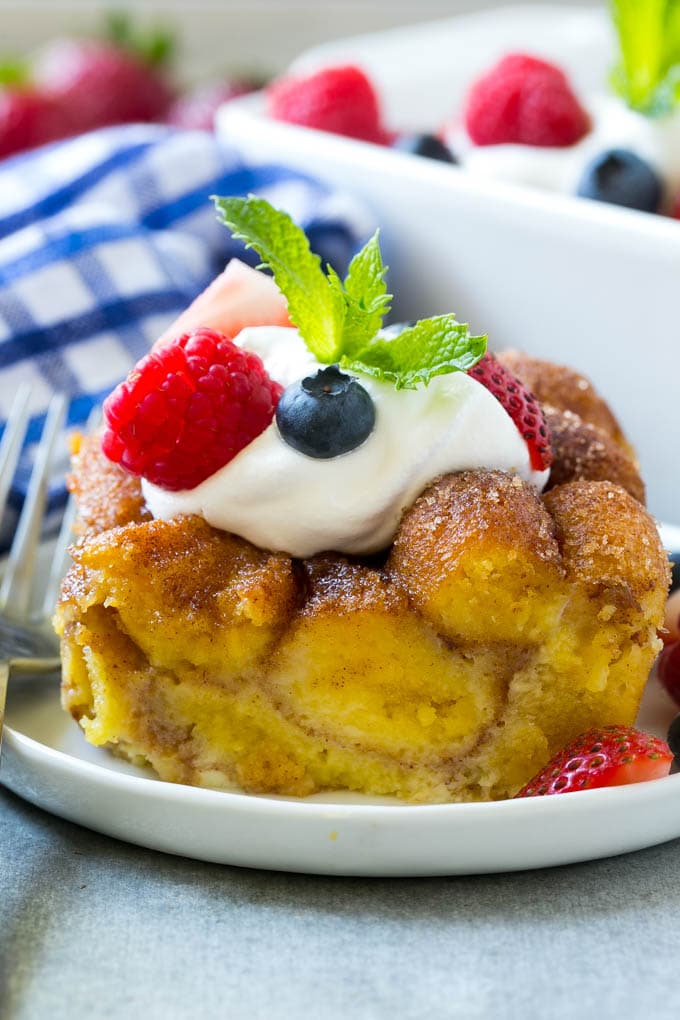Donut Bread Pudding Recipe | Easy Bread Pudding | Cinnamon Donuts | Make Ahead Breakfast Recipe #breadpudding #donuts #donutholes #breakfast #edsug Slice of donut bread pudding topped with whipped cream and berries.