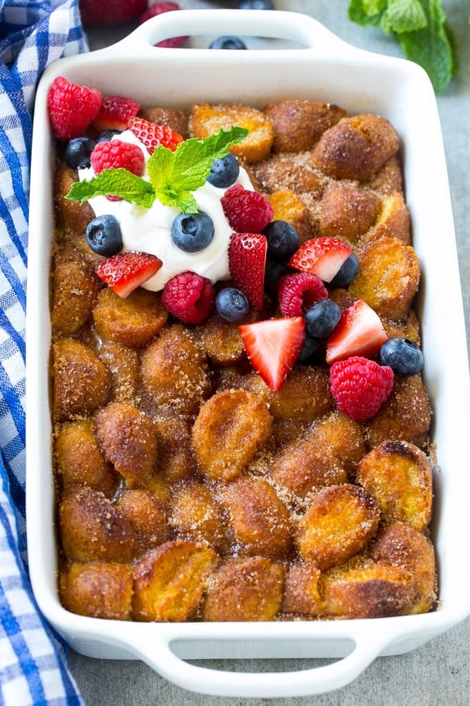 Donut Bread Pudding Recipe | Easy Bread Pudding | Cinnamon Donuts | Make Ahead Breakfast Recipe #breadpudding #donuts #donutholes #breakfast #edsug A tray of donut bread pudding garnished with whipped cream and berries.