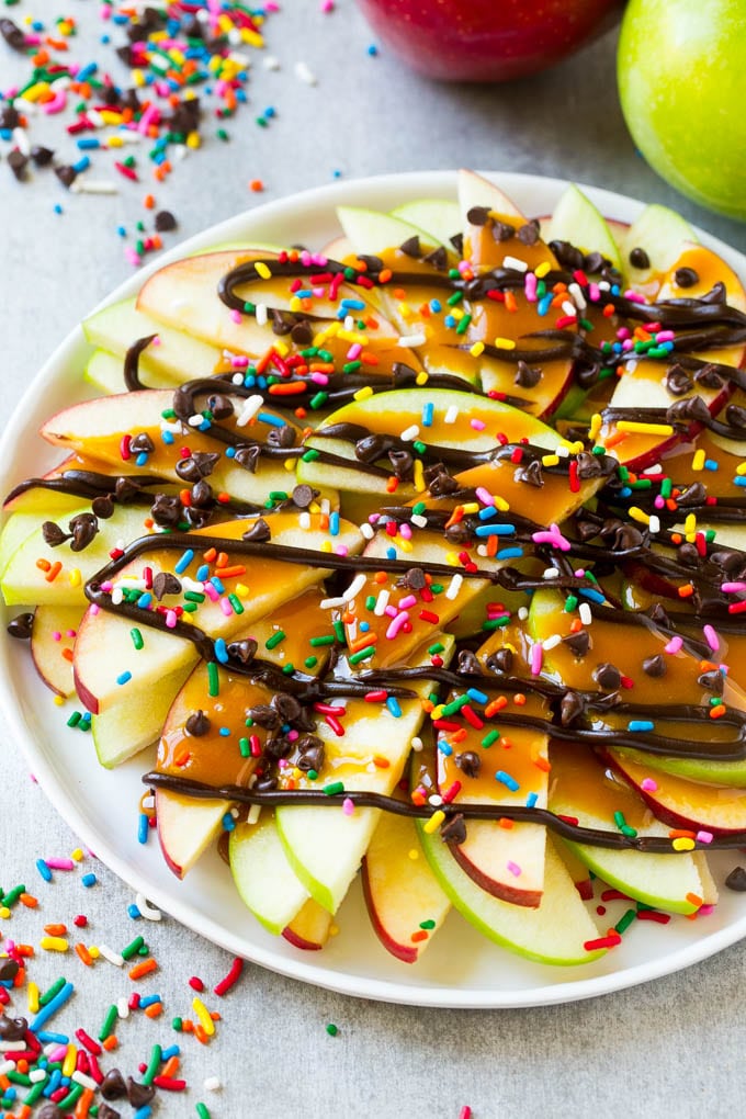 Apple Nachos Recipe | After School Snack | Caramel Apples #apple #apples #caramelapple #snack #dessert #edsug A plate of sliced apple nachos topped with caramel and chocolate sauces, rainbow sprinkles and mini chocolate chips