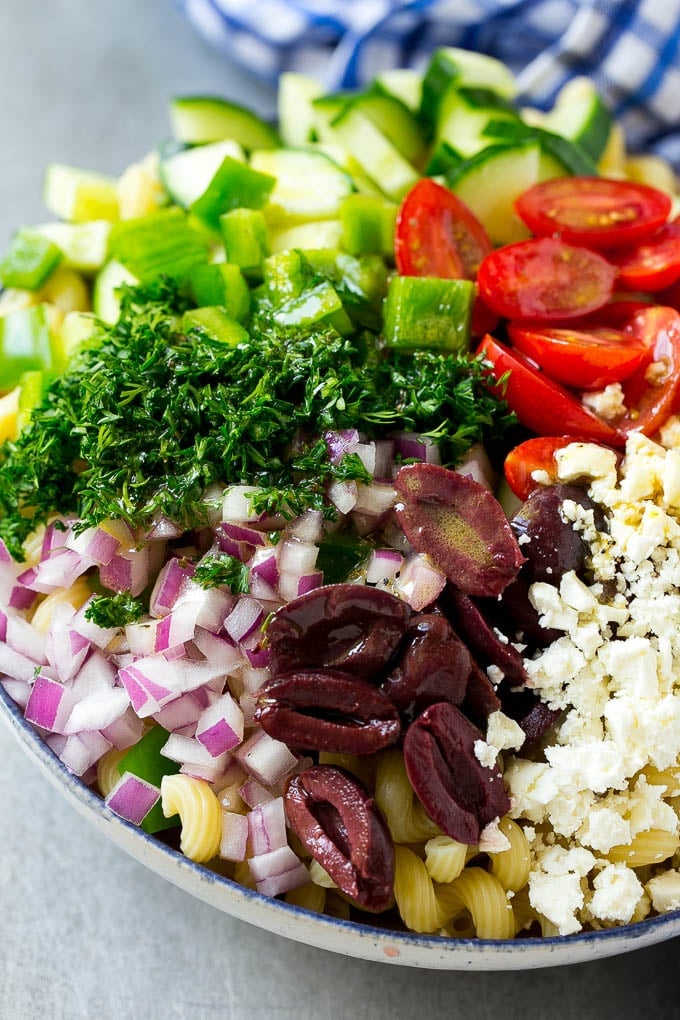 Greek Pasta Salad | Easy Pasta Salad | Vegetable Pasta Salad #pasta #salad #greek #cucumber #tomato #vegetarian #dinner #edsug A bowl of pasta with red onion, kalamata olives, bell pepper and tomatoes, with a drizzle of Greek dressing.