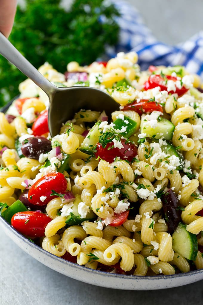 Greek Pasta Salad | Easy Pasta Salad | Vegetable Pasta Salad #pasta #salad #greek #cucumber #tomato #vegetarian #dinner #edsug A bowl of Greek pasta salad with a serving spoon in it.