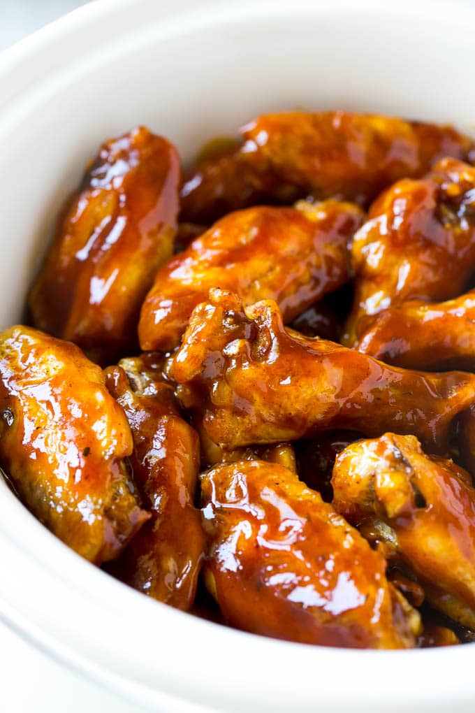 Slow Cooker Barbecue Chicken Wings | Crock Pot Chicken Wings | Barbecue Chicken Wings | Easy Chicken Wings #chickenwings #slowcooker #crockpot #bbqchicken #partywings #appetizer #edsug Slow cooker chicken wings coated in sauce in a white crock pot.