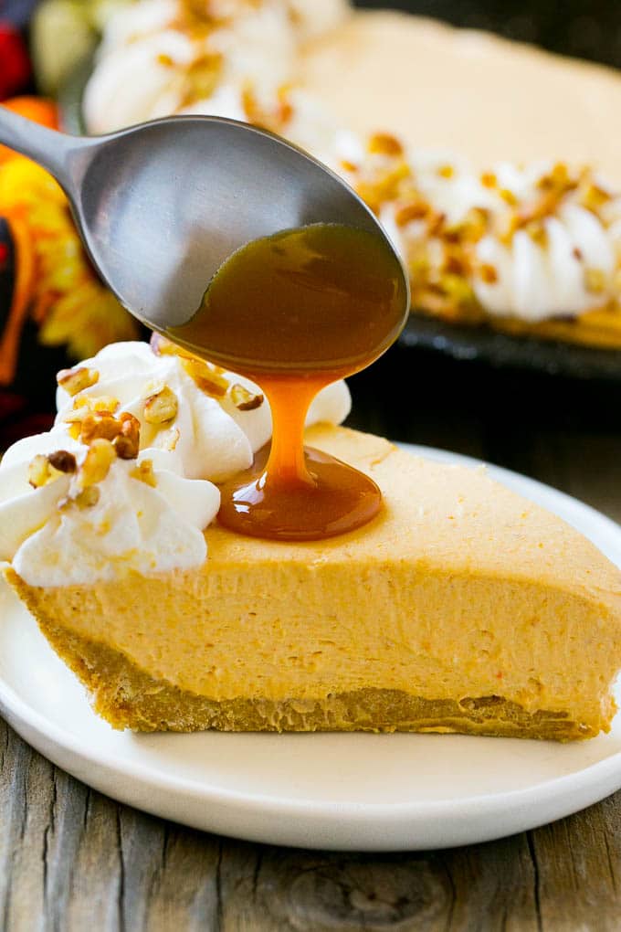 No Bake Pumpkin Cheesecake Recipe | Pumpkin Cheesecake | No Bake Cheesecake | Thanksgiving Dessert | Pumpkin Dessert #nobake #cheesecake #pumpkin #pumpkinpie #pumpkincheesecake #nobakecheesecake #dessert #edsug A spoon pouring caramel over a slice of pumpkin cheesecake.