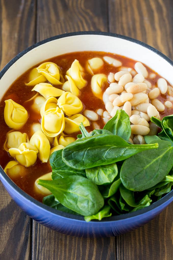 Tortellini Soup Recipe | Sausage Soup | Italian Soup #soup #sausage #pasta #tortellini #dinner #edsug A pot with ingredients like spinach leaves and white beans.