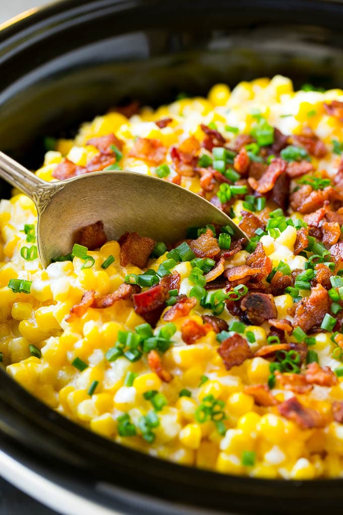 Slow Cooker Creamed Corn Recipe | Easy Creamed Corn Recipe | Slow Cooker Creamed Corn with Bacon | Southern Creamed Corn | Creamed Corn with Cream Cheese #creamedcorn #corn #bacon #crockpot #slowcooker #dinner #edsug A serving spoon in a crock pot full of creamed corn.
