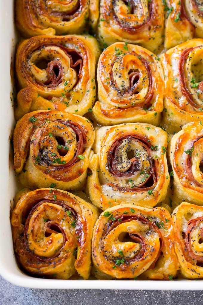 Ham and Cheese Pinwheels Recipe | Ham and Cheese Roll Ups | Ham and Cheese Rolls | Ham and Cheese Bread Rolls #ham #cheese #appetizer #pinwheels #edsug Ham and cheese pinwheels in a baking dish topped with parsley.