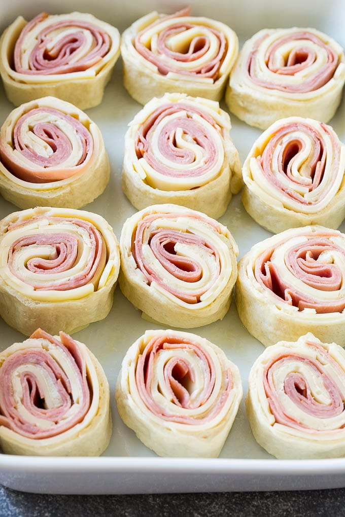 Ham and Cheese Pinwheels Recipe | Ham and Cheese Roll Ups | Ham and Cheese Rolls | Ham and Cheese Bread Rolls #ham #cheese #appetizer #pinwheels #edsug Rolled up ham, cheese and pizza dough circles in a baking dish.