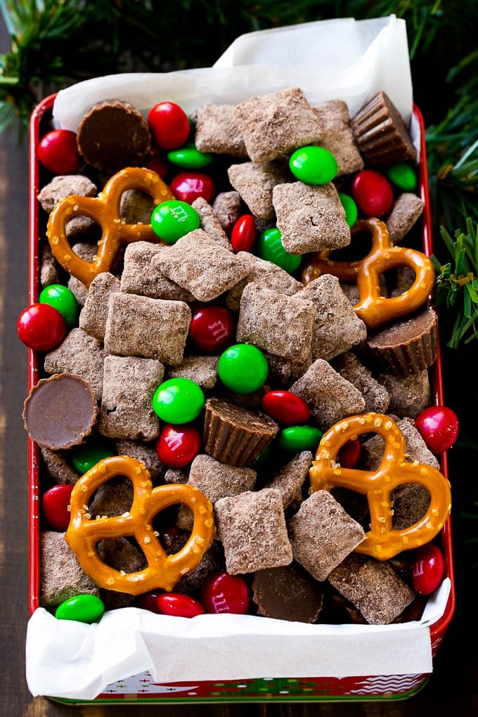 Reindeer Chow | Christmas Chex Mix | Christmas Muddy Buddies | Holiday Chex Mix #chex #chexmix #christmas #holiday #muddybuddies #reindeerchow #snack #edsug A tin of reindeer chow with chocolate coated chex, M&M's and pretzels.