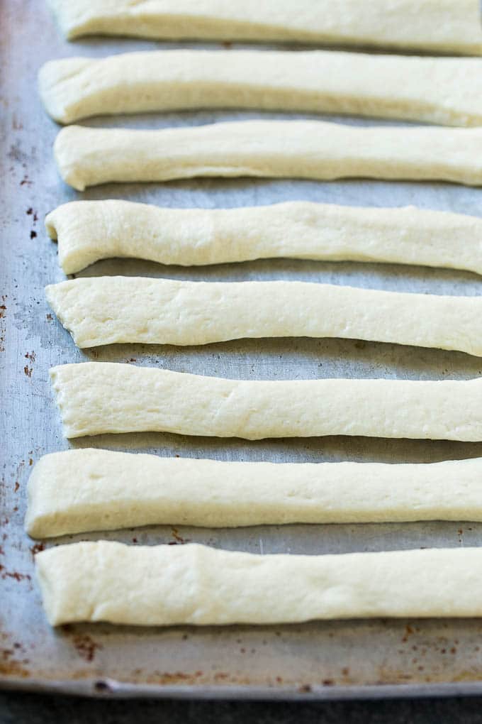 Garlic Knots Recipe | Garlic Rolls | Garlic Butter Rolls | Garlic Bread Recipe #garlic #garlicbread #garlicknots #breadsticks #edsug Strips of pizza dough on a sheet pan that are ready to be tied up.