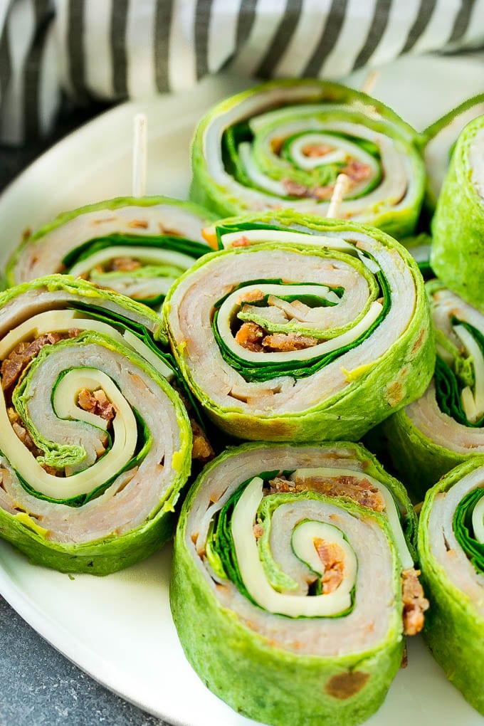 Turkey Roll Ups Recipe | Turkey Pinwheel Sandwiches | Turkey Roller Sandwiches #turkey #avocado #sandwich #lunch #appetizer #edsug Turkey roll up sandwiches filled with cheese, avocado, bacon, turkey and spinach and stacked on a plate.