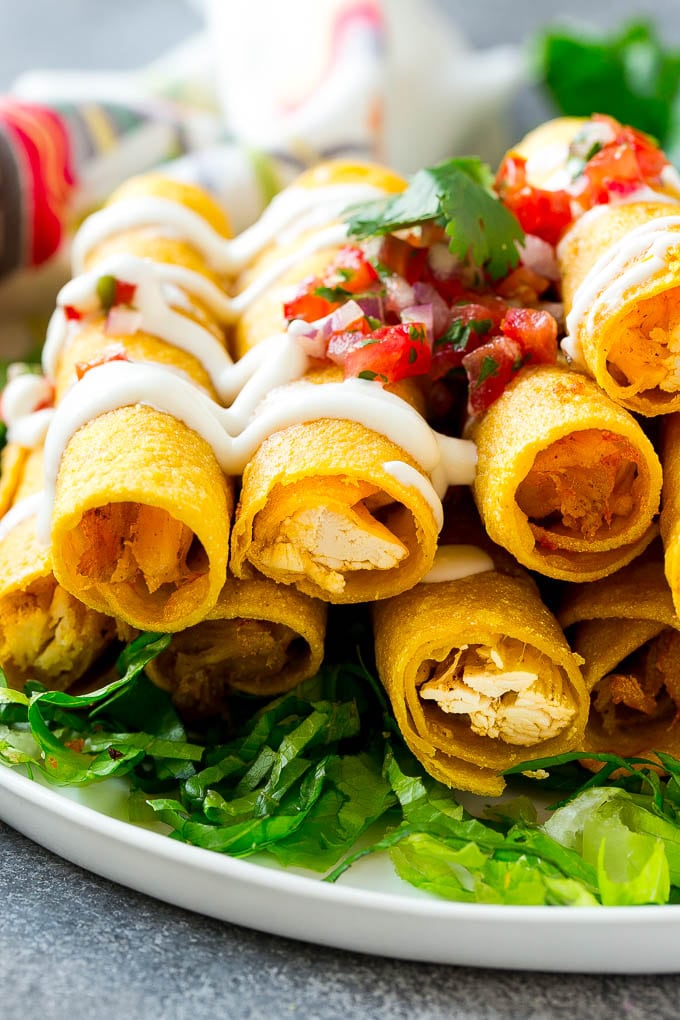 Chicken Taquitos Recipe | Baked Chicken Taquitos | Fried Chicken Taquitos | Mexican Appetizer | Chicken Tortillas #taquitos #chicken #appetizer #tortillas #mexicanfood #edsug A plate of chicken taquitos on a bed of lettuce, topped with sour cream and pico de gallo.