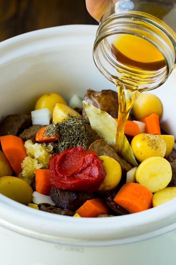 Slow Cooker Beef Stew Recipe | Crockpot Beef Stew #stew #soup #beef #slowcooker #crockpot #dinner #edsug Broth being poured into a slow cooker filled with beef and vegetables.