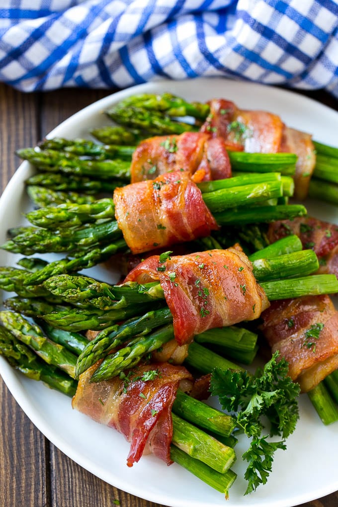 Bacon Wrapped Asparagus Recipe | Roasted Asparagus | Asparagus Side Dish #asparagus #bacon #sidedish #dinner #edsug A plate of bacon wrapped asparagus bundles garnished with parsley.