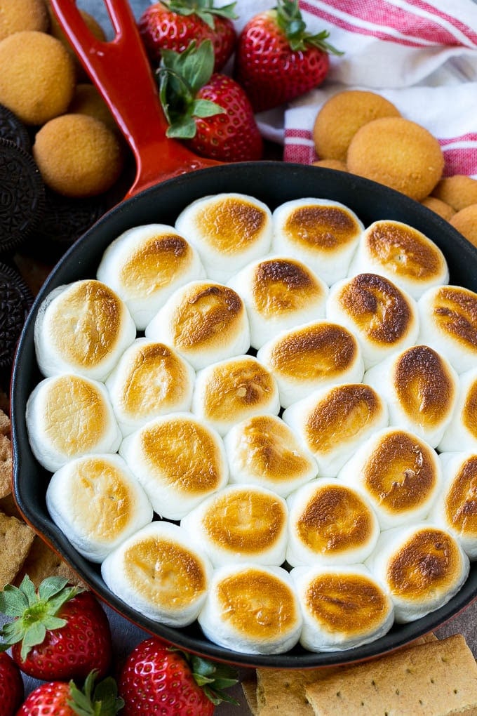 S'mores Dip Recipe | S'mores Skillet | Baked S'mores #smores #dip #chocolate #marshmallow #dessert #edsug A skillet of s'mores dip with melted chocolate chips and toasted marshmallows, surrounded by graham crackers, cookies and strawberries.