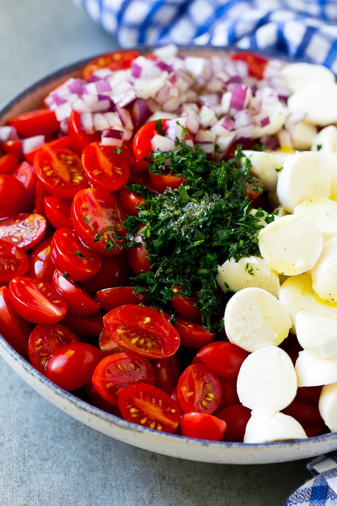 Cherry Tomato Salad Recipe | Tomato Mozzarella Salad | Caprese Salad | Tomato Salad #tomatoes #salad #tomatosalad #caprese #edsug Cherry tomatoes, herbs, mozzarella balls and red onion drizzled with dressing in a bowl.