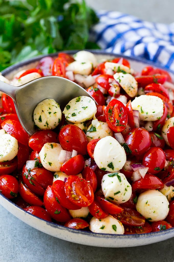 Cherry Tomato Salad Recipe | Tomato Mozzarella Salad | Caprese Salad | Tomato Salad #tomatoes #salad #tomatosalad #caprese #edsug A bowl of cherry tomato salad with a serving spoon in it.