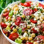 A bowl of chickpea salad with tomatoes, cucumber, avocado, feta cheese and herbs.