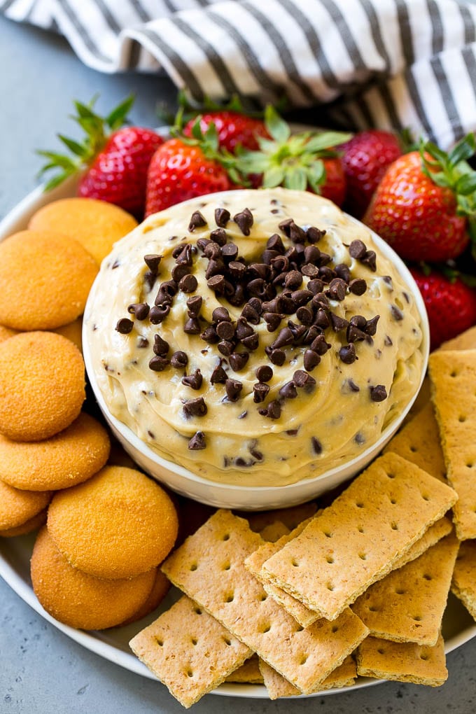 Cookie Dough Dip Recipe | Edible Cookie Dough | Chocolate Chip Cookie Dip #cookies #dip #cookiedough #dessert #snack #edsug A bowl of cookie dough dip topped with chocolate chips and served with cookies and fruit for dipping.