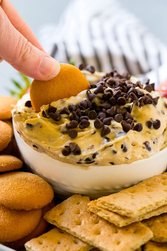 Cookie Dough Dip Recipe | Edible Cookie Dough | Chocolate Chip Cookie Dip #cookies #dip #cookiedough #dessert #snack #edsug A cookie scooping into a bowl of dip.