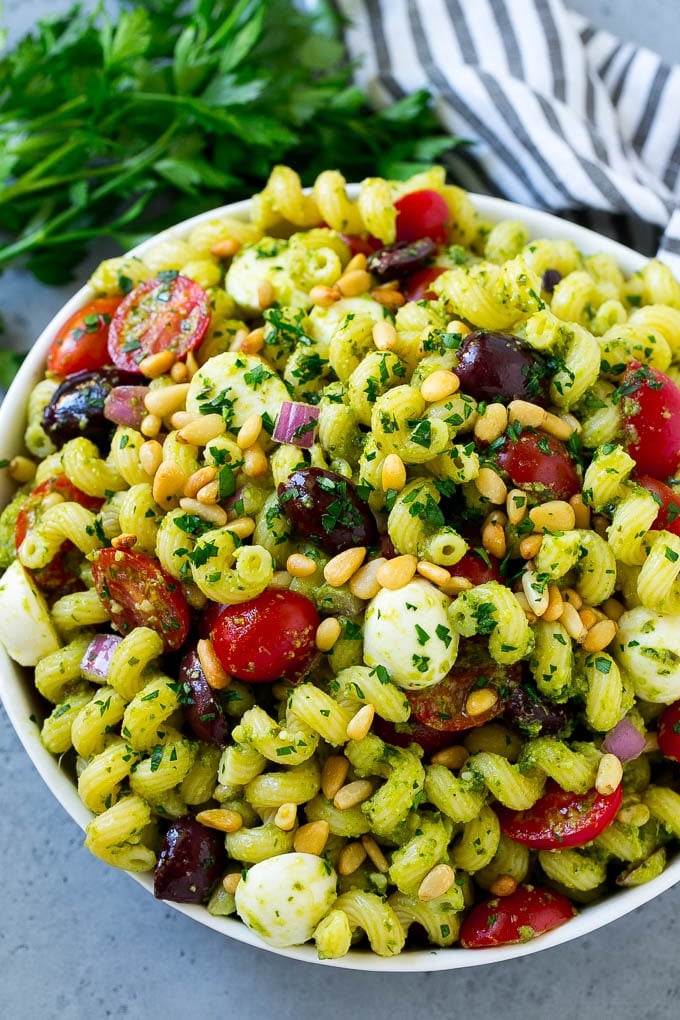 Pesto Pasta Salad | Italian Pasta Salad | Easy Pasta Salad #pasta #salad #pesto #olives #tomatoes #edsug A bowl of pesto pasta salad topped with pine nuts and chopped parsley.