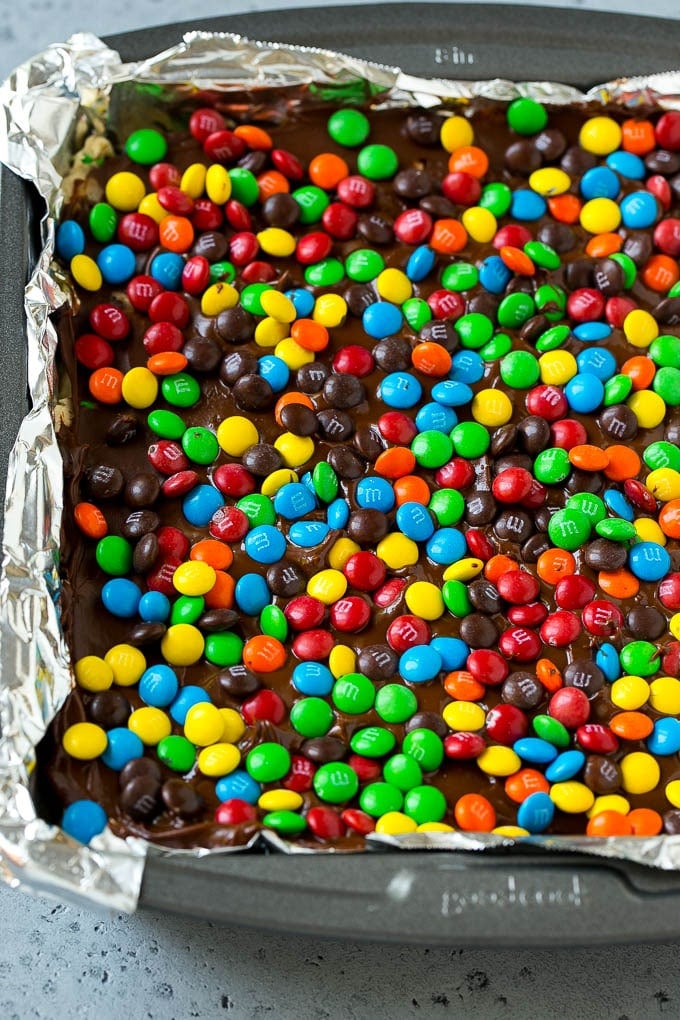 A pan of cookie dough bars topped with chocolate and miniature M&M's.