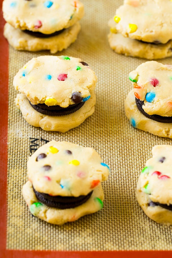 Oreo Stuffed Cookies Recipe | M&M's cookies | Stuffed Cookies #cookies #chocolate #oreos #dessert #baking #edsug Cookie dough sandwiched around Oreos on a baking sheet.