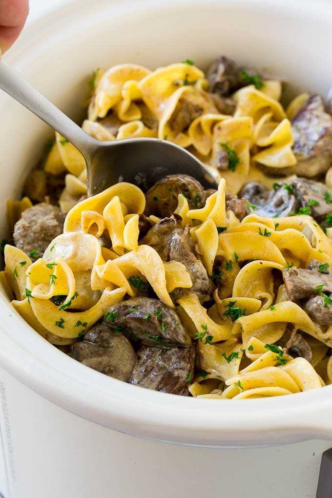 Slow Cooker Beef Stroganoff Recipe | Crock Pot Beef Stroganoff | Beef Recipe #slowcooker #crockpot #beef #mushrooms #pasta #dinner #edsug A crock pot of beef stroganoff with a serving spoon in it.