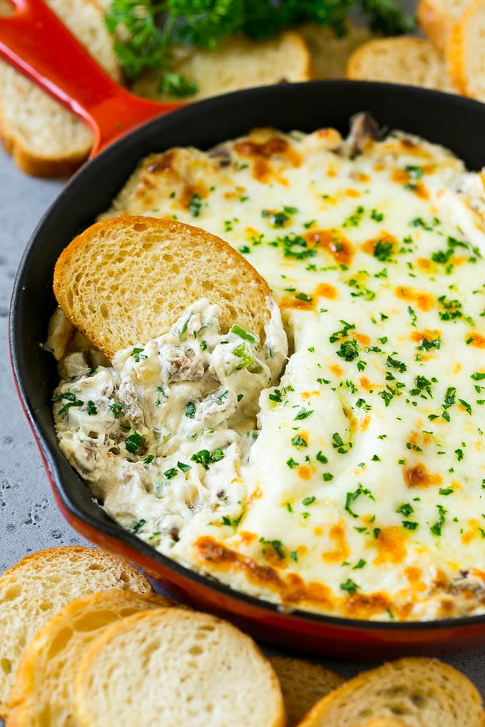 Philly Cheesesteak Dip Recipe | Cheesy Dip | Baked Cheese Dip #steak #dip #appetizer #cheese #edsug Philly cheesesteak dip with a baguette piece scooping some dip out.