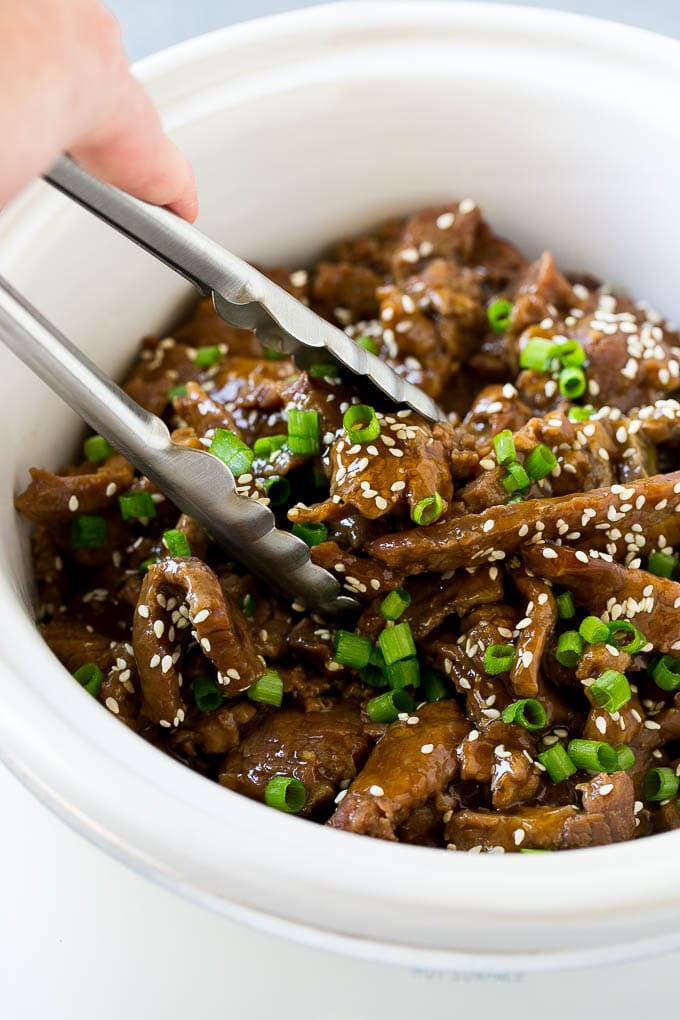 Slow Cooker Korean Beef Recipe | Korean Beef | Flank Steak Recipe #dinner #beef #slowcooker #crockpot #asian #edsug A crock pot of Korean beef with serving tongs in it.
