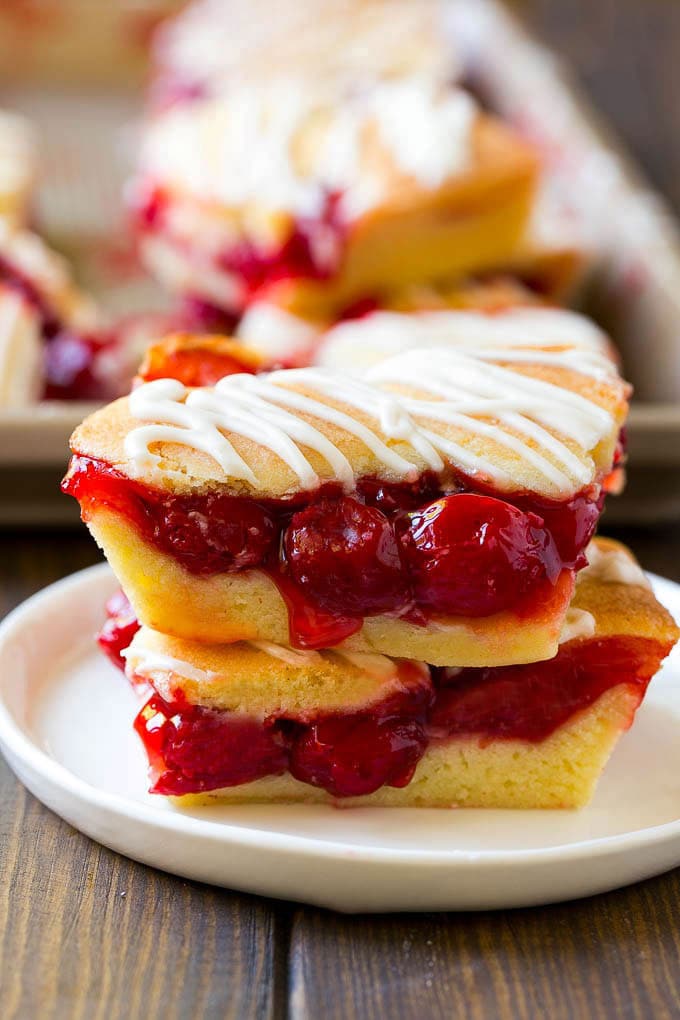 Cherry Bars Recipe | Cherry Pie Bars | Cherry Cookies | Bar Cookies #cookies #bars #cherry #baking #dessert #sweets #edsug Two cherry bars on a plate with a pan of bars in the background.