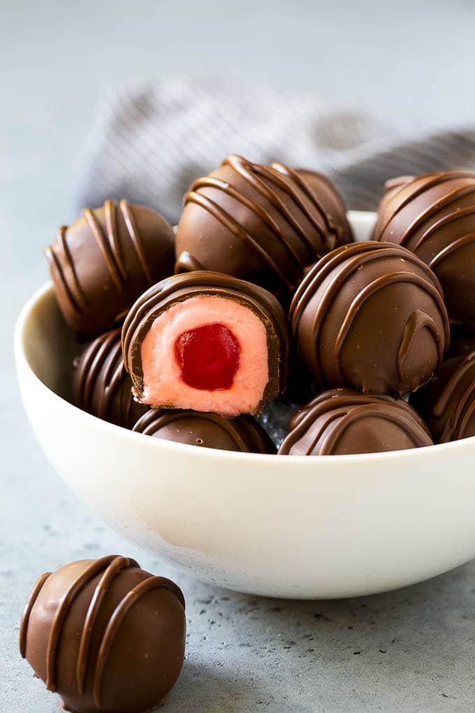 Chocolate Covered Cherries Recipe | Cherry Cordials | Cherry Candy #chocolate #candy #dessert #cherry #sweets #edsug A bowl of chocolate covered cherries with one cut open.