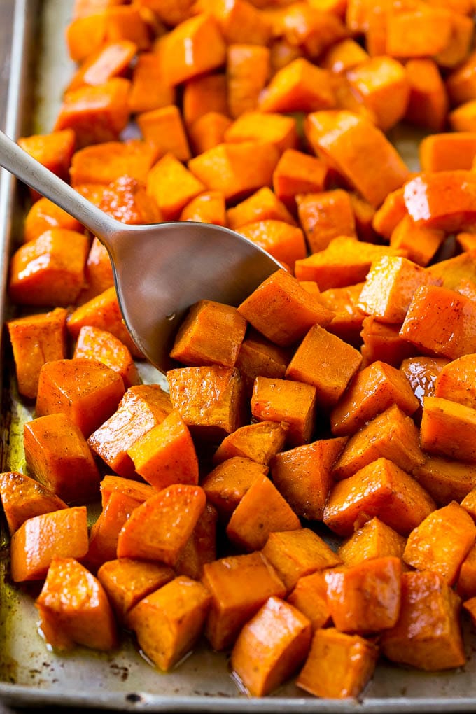 Maple Roasted Sweet Potatoes Recipe | Easy Sweet Potatoes | Baked Sweet Potatoes | Sweet Potato Side Dish #sweetpotatoes #cinnamon #maple #butter #fall #sidedish #dinner #edsug A sheet pan of baked yams flavored with maple and cinnamon, with a serving spoon in them.