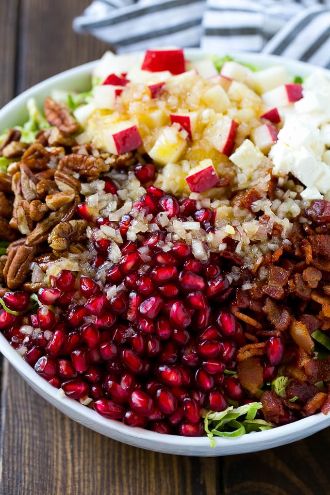 Brussels Sprout Salad Recipe | Shredded Brussels Sprouts Salad | Fall Salad #salad #brusselssprouts #bacon #thanksgiving #pomegranate #apple #dinner #edsug Dressing poured on top of salad that contains sprouts, pomegranate seeds, pecans and bacon.