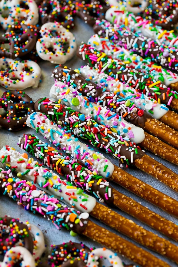 Chocolate Covered Pretzels Recipe | Sprinkle Pretzels | No Bake Dessert #pretzels #chocolate #christmas #sprinkles #candy #edsug A sheet pan with coated twists and rods decorated with rainbow sprinkles.