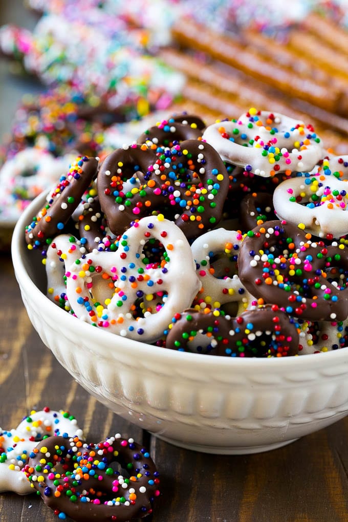 Chocolate Covered Pretzels Recipe | Sprinkle Pretzels | No Bake Dessert #pretzels #chocolate #christmas #sprinkles #candy #edsug A bowl of chocolate covered pretzels decorated with rainbow sprinkles.