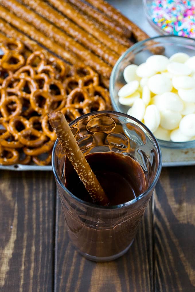 Chocolate Covered Pretzels Recipe | Sprinkle Pretzels | No Bake Dessert #pretzels #chocolate #christmas #sprinkles #candy #edsug A rod in a glass full of melted chocolate.