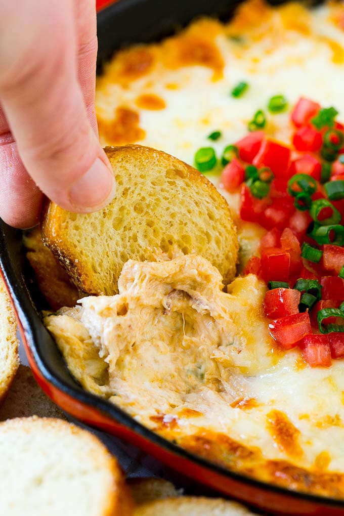 Crab Dip Recipe | Hot Crab Dip | Seafood Dip #dip #crab #seafood #appetizer #edsug #cheese A hand scooping out some crap dip with a crostini toast.
